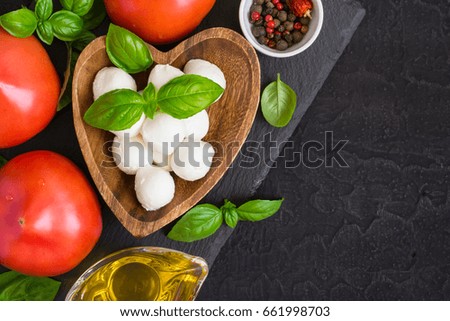 Mozzarella cheese, tomatoes and basil on a black stone table. Top view with copy space