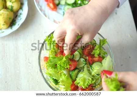 Female hands are cooking vegetable salad at the kitchen. Close-up picture, selective focus.