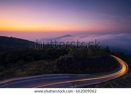 Mountain fog and light line on the road from cars during the sunrise 