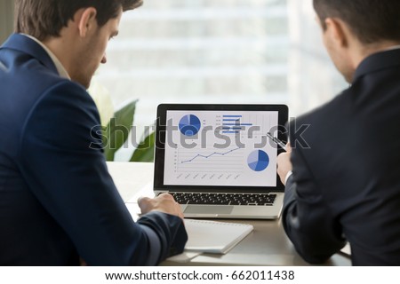 Rear view at two businessmen analyzing stats financial data on pc laptop, pointing at screen with rising graph and charts, discussing company growth, using easy accounting software for small business Royalty-Free Stock Photo #662011438