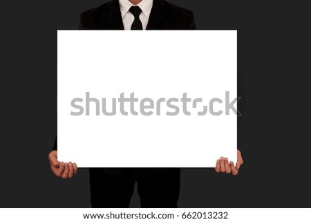 Businessman in black suit holding blank white board on gray background.