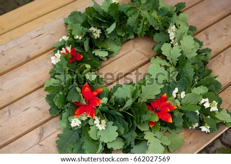 Wreath from oak leaves with jasmine and red flowers on wooden background. Midsummer in Latvia. Celebration of Ligo feast in June Royalty-Free Stock Photo #662027569