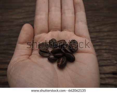 Hand holding coffee bean on wooden background.