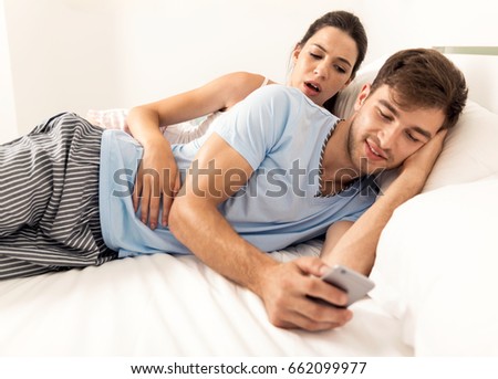 Addicted young man on bed texting  while woman looks angry