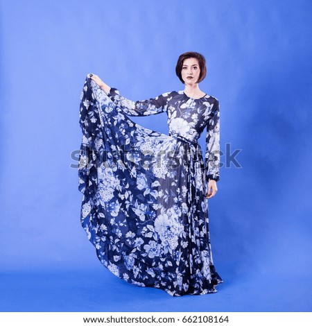 Gorgeous woman with long flying dress on blue background in studio photo. Elegance and beauty