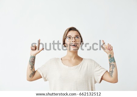 Young beautiful girl in glasses smiling pointing fingers up over white background.