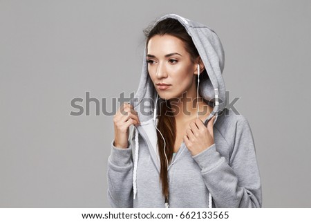Portrait of attractive sportive girl in hood and headphones posing over white background.