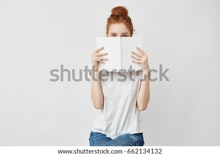 Beautiful foxy girl hiding face behind book looking at camera.