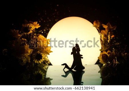 Silhouettes of toy couple dancing under the Moon at night. Figures of man and woman in love dancing at moonlight with fog