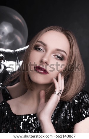 Close up fashion portrait of a young beautiful elegant girl with bright party make up in evening black sequin top. She is keeping silver stars balloons in her hand. Girl at the party.