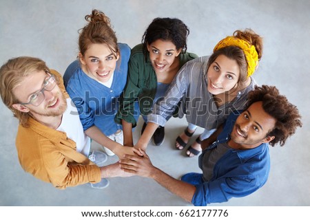 View from above of five multiracial people standing together stacking their hands looking happily symbolyzing their friendship and support. International fellowship. Mixed race people community Royalty-Free Stock Photo #662177776