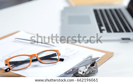 Closeup of white desktop with laptop, glasses, coffee cup, notepads and other items on blurry city background