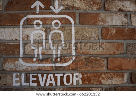 An Elevator sign hangs on red brick wall