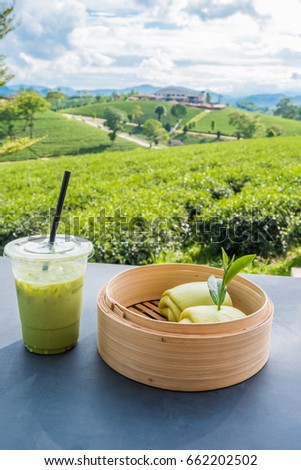 Matcha iced green tea in clear plastic glass and steamed bun table with tea plantation background at Choui Fong Chiang Rai province, Thailand. Royalty-Free Stock Photo #662202502