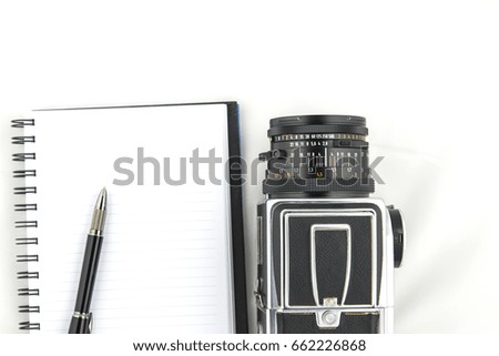 The photo shows a medium format camera with pen and notebook on white background