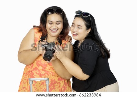 Two cheerful women looking their photo at digital camera, isolated on white background  