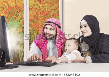 Picture of middle eastern family wearing Muslim clothes using a computer together with autumn background on the window