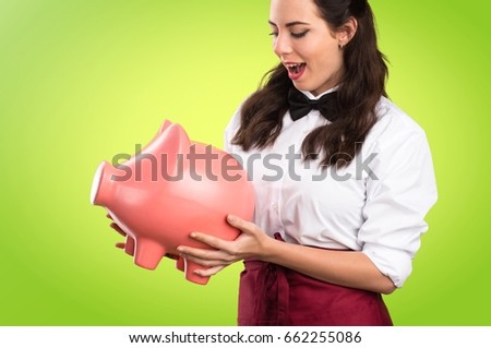 Young beautiful waitress holding a piggybank on colorful background