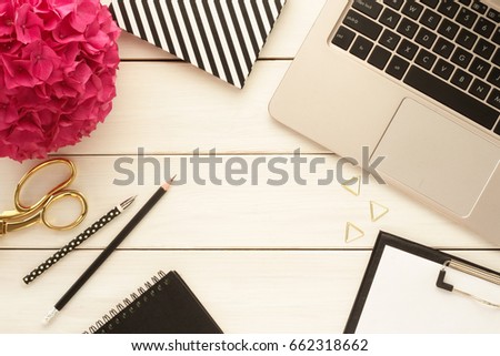 Office desk table with computer, supplies and pink hydrangea flower. White wooden background. Top view.