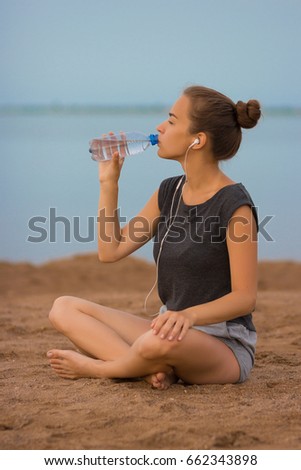 Selective focus Sports girl drinks water during a workout on the beach. The girl drinks water during fitness outdoors