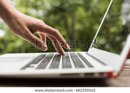 Young beautiful woman hand press keyboard on computer laptop on old wooden table at the garden in the morning. Nature green background with bokeh.