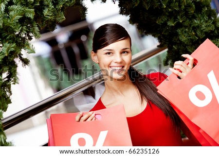 Happy girl holds red paperbags with symbol of sale in market