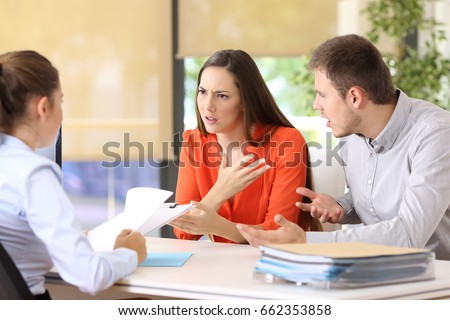 Angry couple arguing telling their problems sitting in a desktop of a marriage counseling or office Royalty-Free Stock Photo #662353858