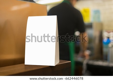  Mock up Menu frame on Table in Bar restaurant or coffee shop ,Stand for booklets with white sheets of paper acrylic tent card on cafeteria ,barista preparing cup of coffee for customer in background.
