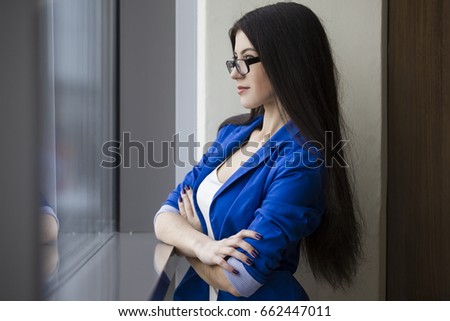 Side view of a beautiful businesswoman in glasses standing with crossed hands and looking in an office window