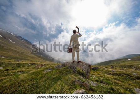 Businessman in a white suit blowing in the horn in the mountains