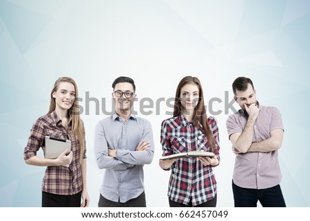 Two women and two men are standing together near a gray wall. One of them is holding an open book and a tablet. Brainstorming. Mock up