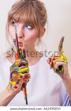 girl painter holding paintbrushes, thinking of composition, with colored hands