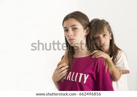 Portrait of two 15 and 10 year old sisters on a white background. It takes with natural light that enters through a window.