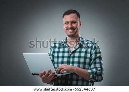 Attractive business man model in green shirt isolated on gray working with laptop, showing something by left hand.