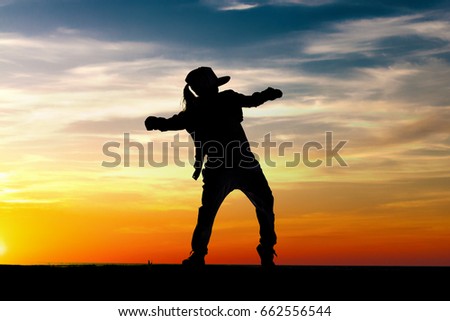 Silhouette of happy little girl dancing on sunset sky background. Copy space.