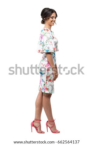 Elegant shy feminine fashion female model in floral dress smiling and looking down. Side view. Full body length portrait isolated on white background.