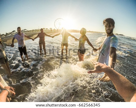 Firsthand view of happy friends having fun on the beach at sunset - Young people playing inside sea water outdoor - Friendship, youth,travel concept - Soft focus on right man face - Contrast filter Royalty-Free Stock Photo #662566345