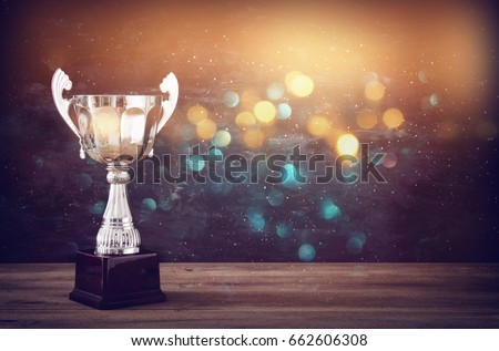 low key image of trophy over wooden table and dark background, with abstract glitter lights