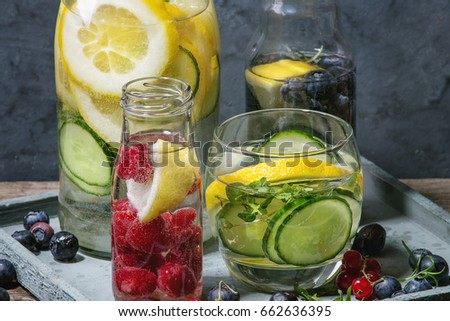 Citrus cucumber berries blueberry and raspberry sassy sassi water for detox in glass bottles on wooden blue background. Clean eating, healthy lifestyle concept, sunlight
