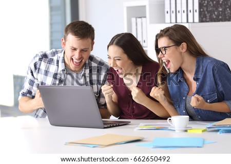 Three excited employees reading good news on line in a laptop sitting in a desktop at office Royalty-Free Stock Photo #662650492