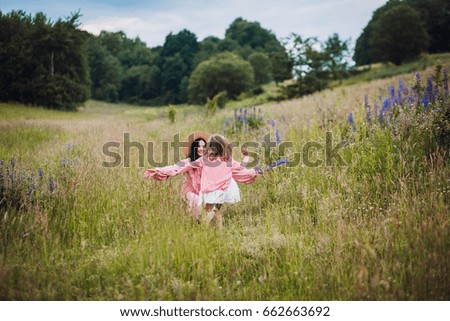 Mom and daughter in pink dresses run barefooted on the field