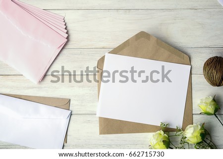 Top view of envelope and blank greeting card with rose flowers on white wooden background.