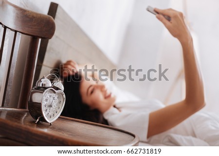 Silver heart shaped alarm clock with woman taking selfie behind