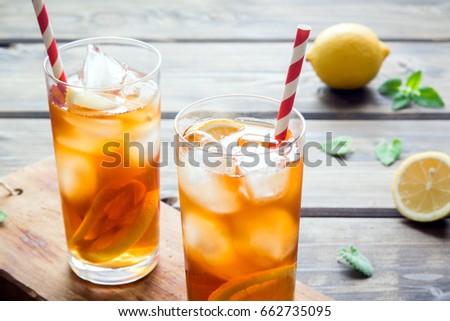 Iced tea with lemon slices, mint and ice cubes on wooden rustic background close up. Homemade refreshing summer drink.