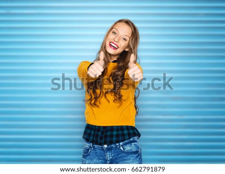 people, gesture and fashion concept - happy young woman or teen girl in casual clothes showing thumbs up over blue ribbed wall background