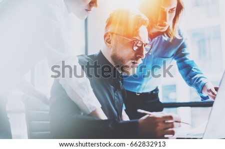 Group of three young coworkers working together at modern coworking office.Teamwork concept.Blurred background.Flares effect.Visual effects.Horizontal