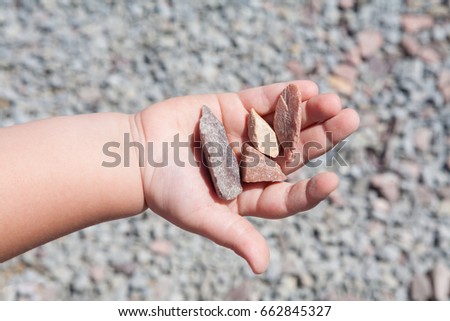 Summer. Sunny day. On the palm of the child are beautiful stones. A picture on the background of rubble. Color gray, red, pink, yellow, gray