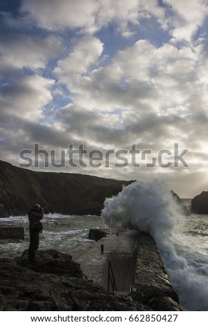 Photographer taking a picture of a wave over breakwater