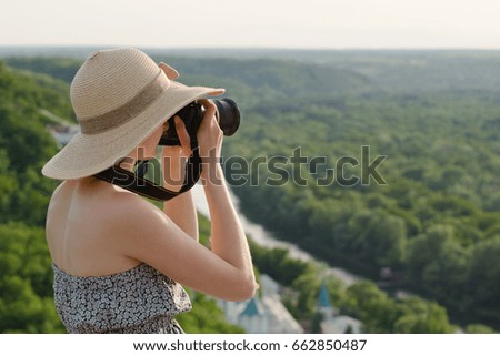 Girl on hill takes pictures against the background of a forest and meandering river