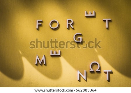 Yellow wall background with latin letters on it randomly fixed composing a phrase: "Forged me not".  Photo taken in Athens, Greece